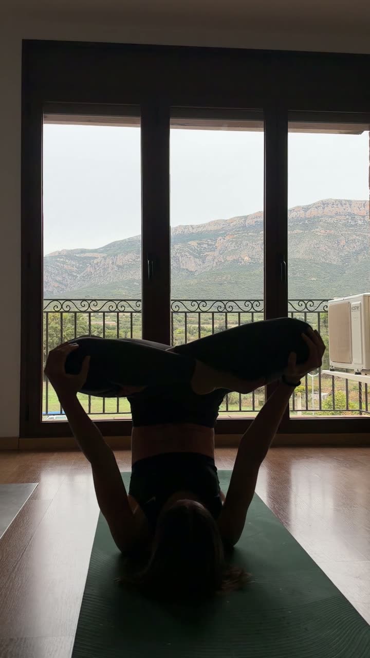 Noel haciendo yoga frente a un ventanal con montañas